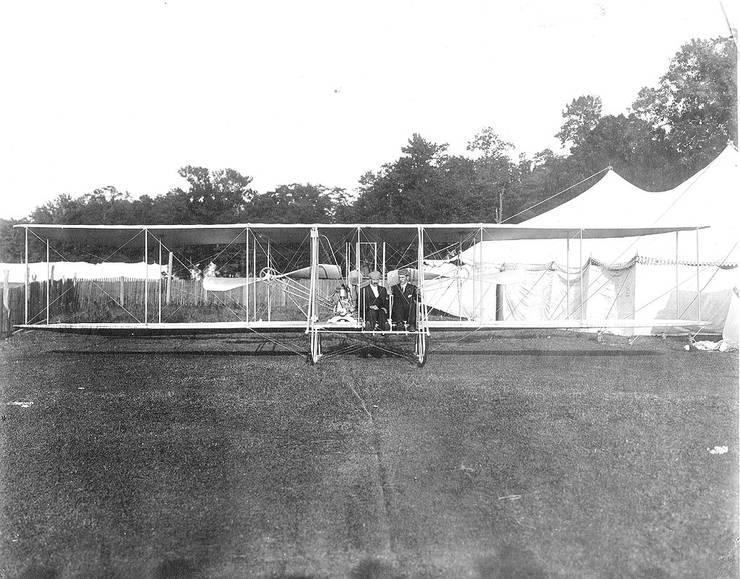 Frank Coffyn (right) and Duval La Chapelle posing in a Wright aircraft in front of tents.