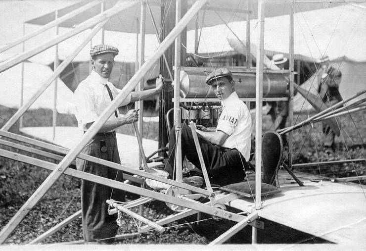 Frank Coffyn and Walter Brookins at an air meet with a Wright transitional aircraft. Brookins appears to be distracted by the photographer while attending to the engine.
