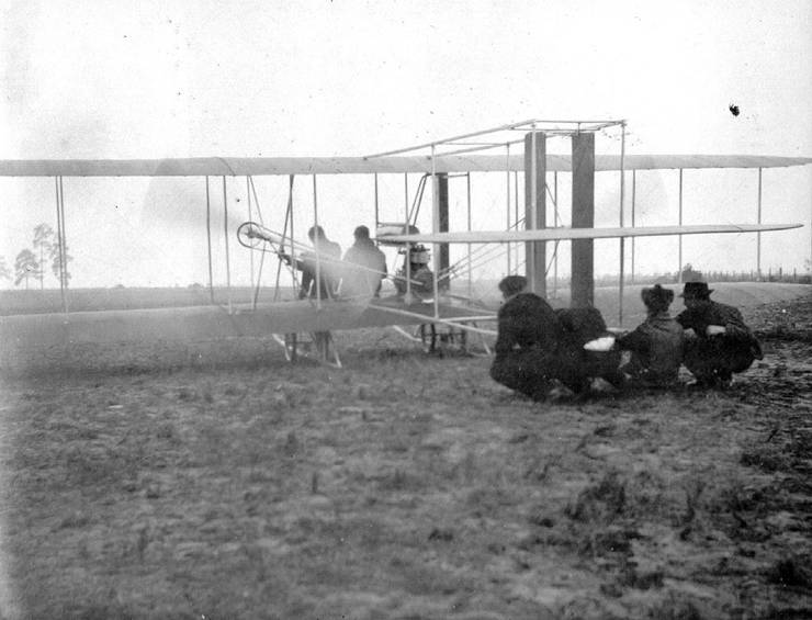 Model B just before launch. The propellers spinning, four men hold the tail boom, Coffyn and passenger aboard.