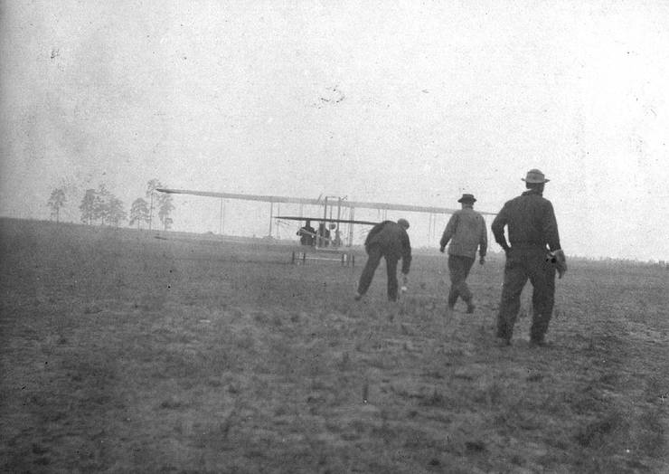 Model B taking off, with three men in view, having just let go of the tail boom.